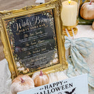 Halloween-themed tabletop decor featuring a gold-framed 'Witch's Brew Dirty Soda Bar' sign, a light blue 'Happy Halloween' card with a jack-o'-lantern, pumpkins, a lit candle, and a tied fabric bow.
