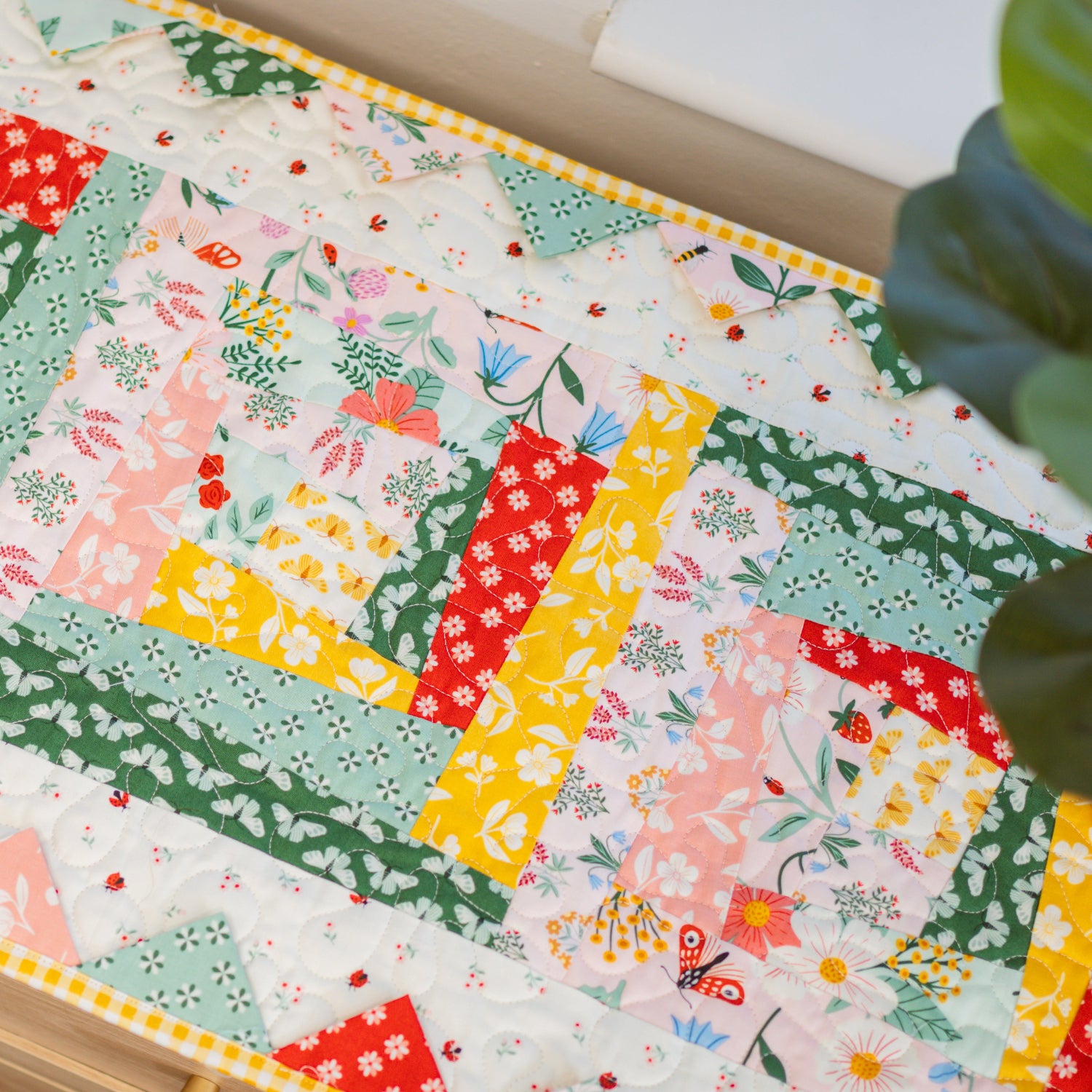 Colorful patchwork quilt on a table with a plant in the corner