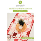 Pink and white patchwork table runner with a plant on a white background, featuring 'my girlfriend's quilt shoppe' branding.
