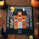 Halloween-themed quilt with haunted house design on a wooden surface with pumpkins and leaves.