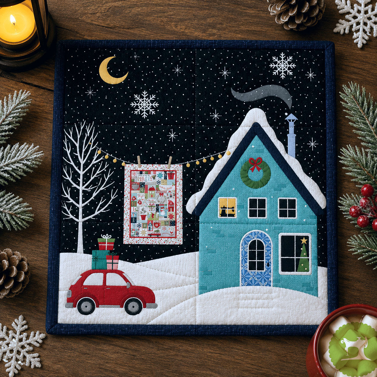 Quilted Christmas scene with a house, car, and tree on a wooden surface.