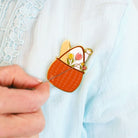 Person inserting a decorative brooch with floral design into a light blue garment.