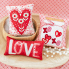 Three decorative pillows with heart designs on a pink textured background
