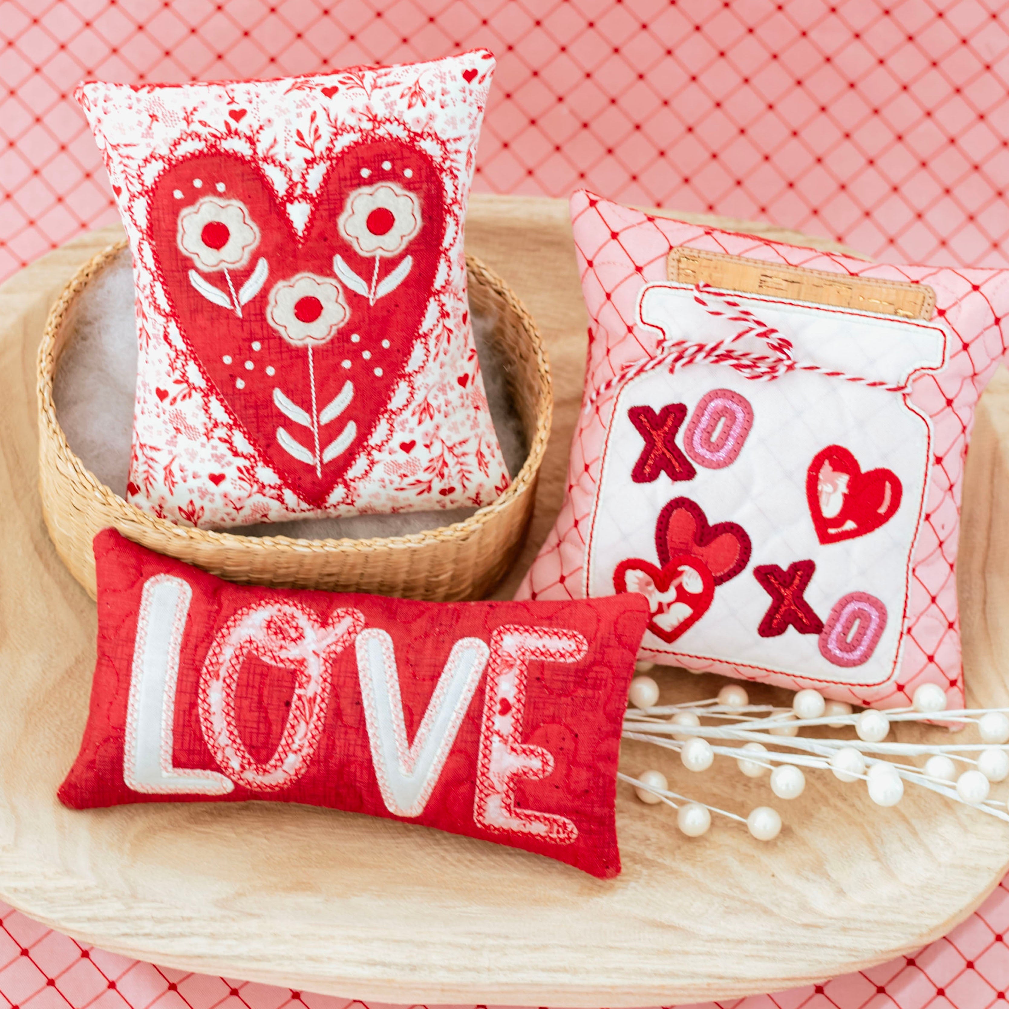 Three decorative pillows with heart designs on a pink textured background