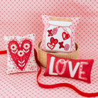 Decorative pillows with heart and 'LOVE' designs on a pink textured background
