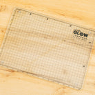 Grid-patterned cutting mat with 'Cutterpillar Glow' branding on a wooden surface