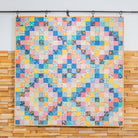 Colorful patchwork quilt hanging on a wall with a wooden panel background