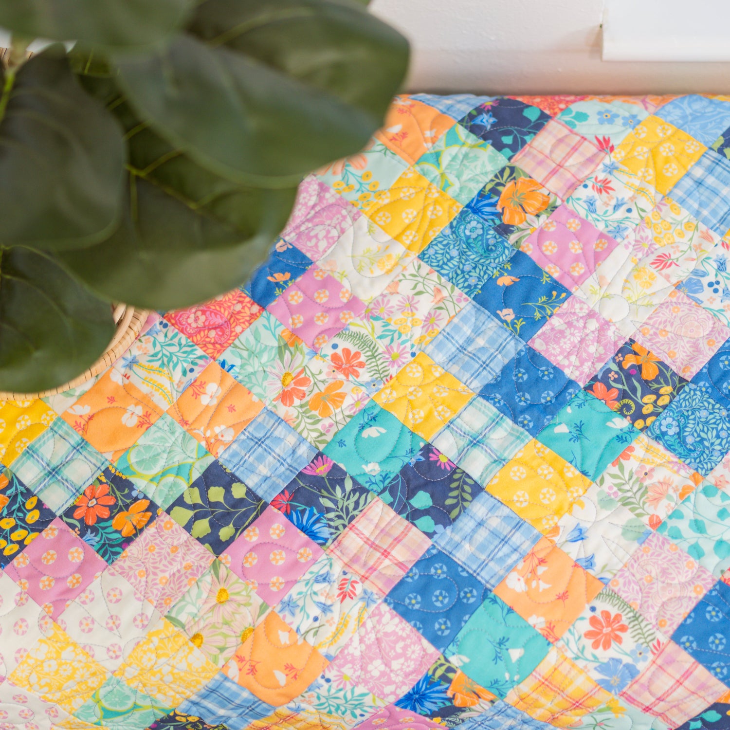 Colorful patchwork quilt with floral patterns on a wooden surface, next to a potted plant.