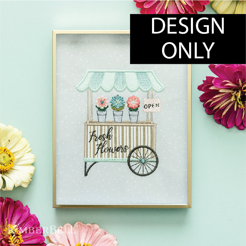 A framed embroidery of a flower cart. 